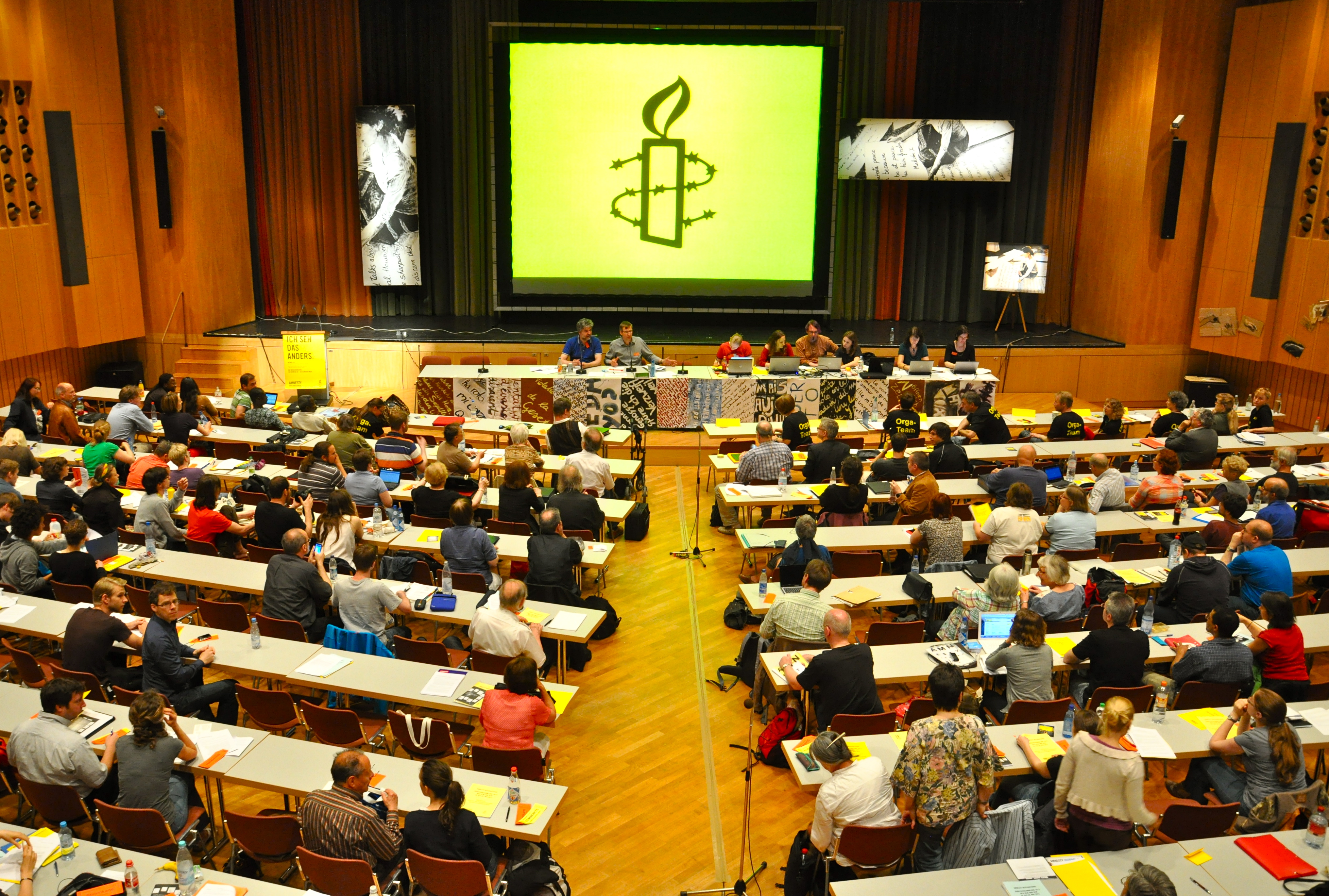 Eine Versammlung oder Sitzung mit acht Sprechern. Auf die Bühne ist das Logo von Amnesty International projiziert.