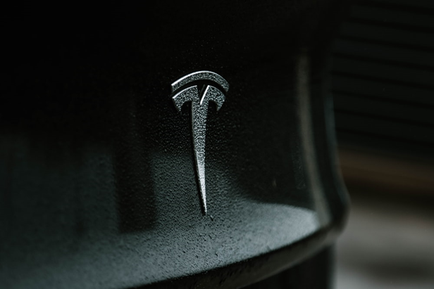 Ein Tesla-Logo auf einem schwarzen, nassen Auto.